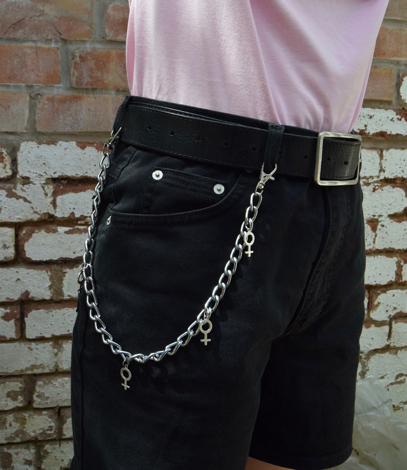 May include: A silver chain with female symbols hanging from a black belt worn over black shorts.