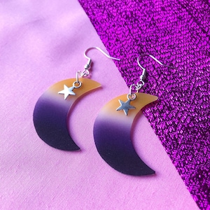 May include: A pair of crescent moon earrings with a yellow, white, and purple ombre effect. Each earring has a small silver star charm.