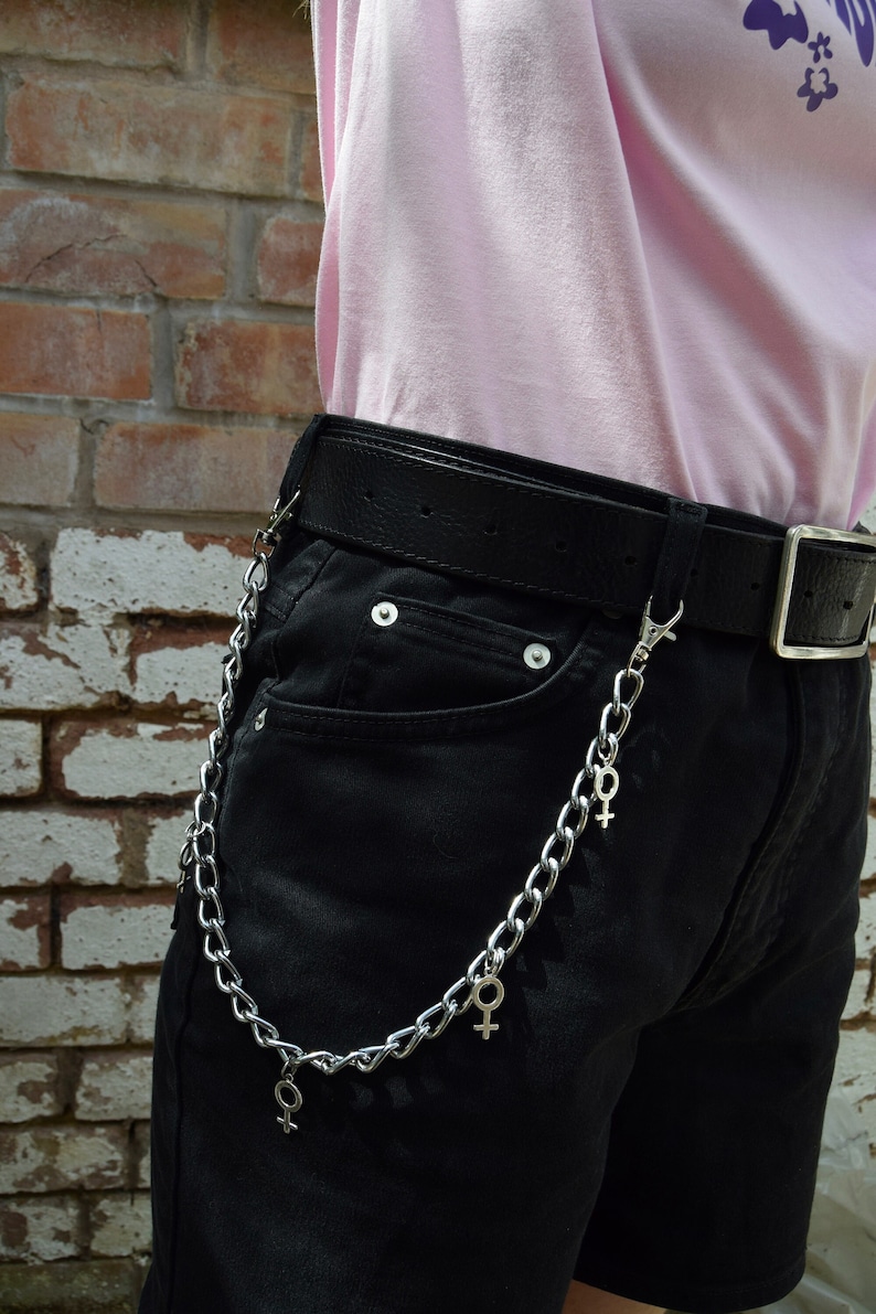 May include: A silver chain with multiple charms in the shape of the female symbol. The chain is attached to a black belt worn around a person's waist.