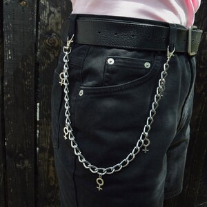 May include: A silver chain with multiple charms hanging from a black belt. The charms are in the shape of the female gender symbol.