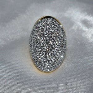 May include: A gold ring with a large oval-shaped stone covered in small, clear rhinestones.