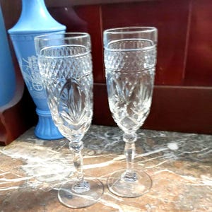 May include: Two clear glass champagne flutes with a cut crystal design. The flutes have a tall, slender stem and a wide bowl.