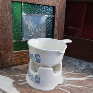 May include: White ceramic fondue pot with a blue floral design. The pot sits on a matching stand with three holes for a candle.