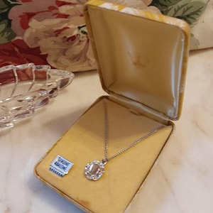 May include: A vintage necklace with a silver chain and a pendant in a gold-colored box. The pendant has a central stone surrounded by a decorative silver frame. The box is open, revealing the necklace. A small tag reads "Genuine Abalone."