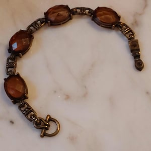 May include: A vintage-style bracelet featuring oval-shaped amber-colored stones set in a bronze-toned metal. The bracelet has a decorative link design and a clasp closure. The stones are faceted, catching the light and adding a touch of elegance.