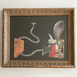May include: A framed collage artwork featuring a variety of textures and colors. The artwork includes a metallic object, a wooden object, a fabric object, and a clear plastic object. The artwork is set against a dark background.