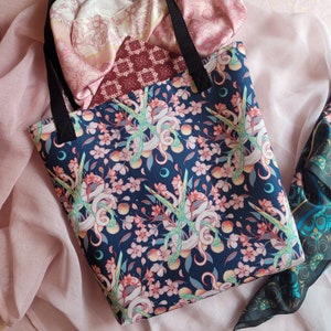 May include: A navy blue tote bag with a floral and snake design. The bag has a black strap and is made of a durable fabric.