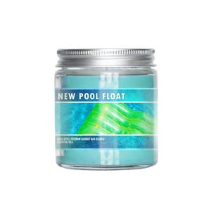 Puede incluir: Un tarro de vidrio transparente con tapa plateada, que contiene una vela de color turquesa. La etiqueta dice "NEW POOL FLOAT" con un diseño azul y verde. La parte inferior de la etiqueta dice "MADE WITH A PREMIUM COCONUT WAX BLEND & ESSENTIAL OILS".