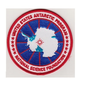 May include: A red, white, and blue embroidered patch with the text "United States Antarctic Program National Science Foundation" and a white outline of the continent of Antarctica with a blue and turquoise sun.