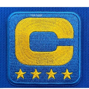 May include: A blue patch with a yellow embroidered letter "C" and four yellow stars. The patch is rectangular with rounded corners and is sewn onto a blue fabric. The text "FAN SHOP" is visible at the top.