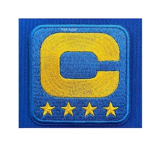May include: A square embroidered patch on a blue mesh fabric featuring a large yellow letter C centered above four small yellow stars. The patch has a blue border and the text FAN SHOP is visible in small letters at the top of the patch design.