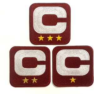 May include: Three maroon embroidered patches with a white "C" and gold stars. The top patch has three stars, the bottom left has two, and the bottom right has one star. The patches are square with rounded corners.