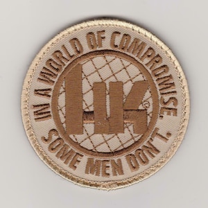May include: A beige embroidered patch with brown stitching. The patch features a stylized image of a city skyline with the text "In a world of compromise, some men don't."