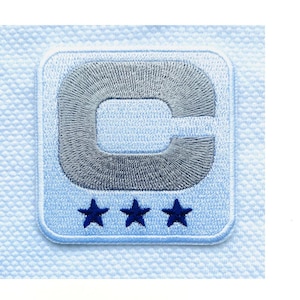 Könnte beinhalten: Ein quadratischer Stickaufnäher mit hellblauem Hintergrund und einem großen, mittig platzierten silber-grauen Buchstaben C. Unter dem Buchstaben sind drei kleine, dunkelblau gestickte Sterne in einer horizontalen Reihe angeordnet.
