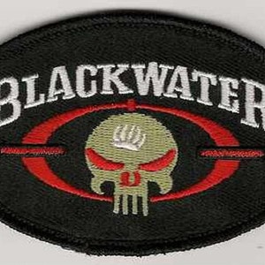 Può includere: Toppa ricamata in bianco e nero con il testo "Blackwater" in bianco e un bersaglio rosso con un teschio al centro. Il teschio è beige con occhi rossi.