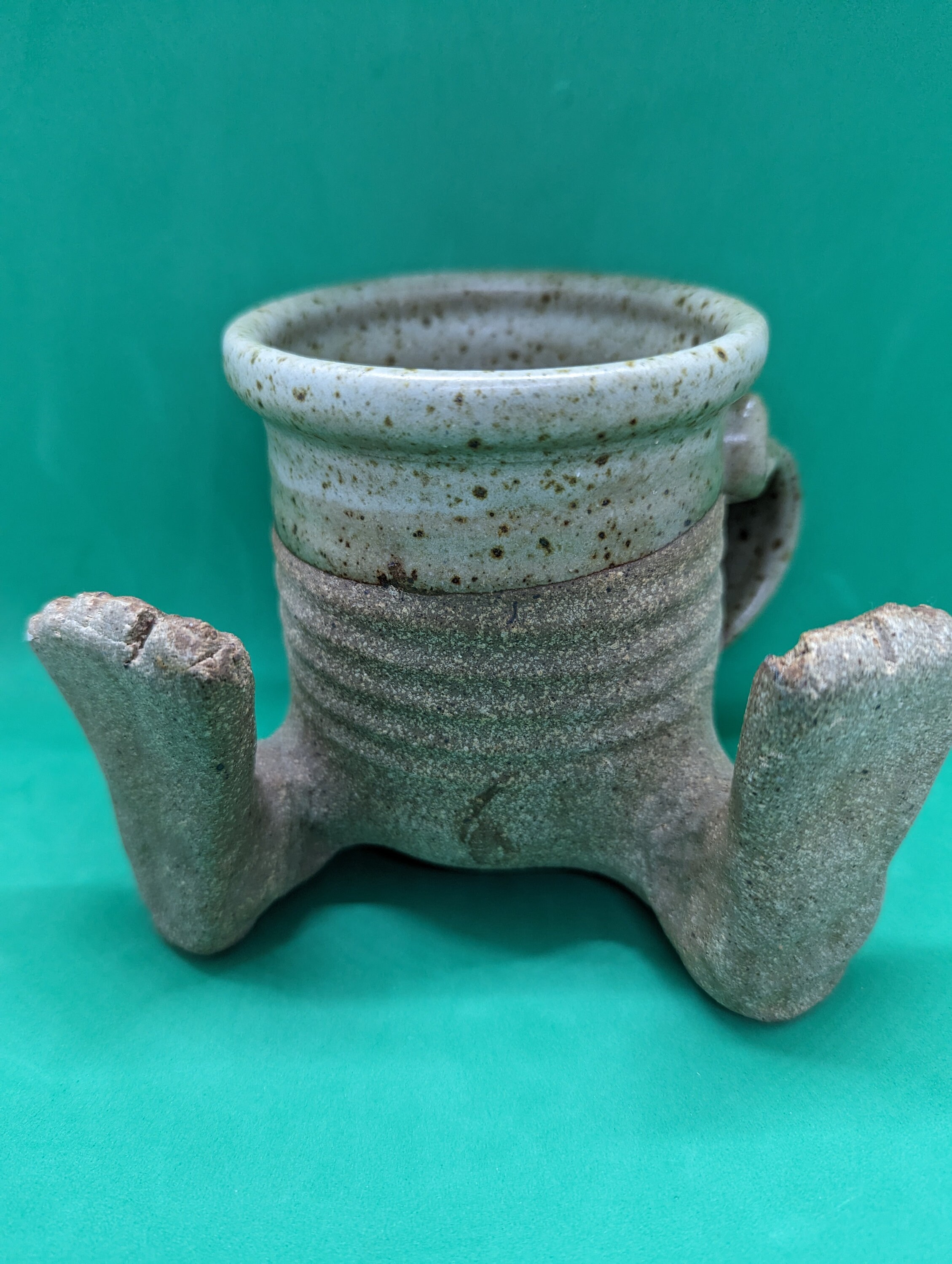 Pottery mug studio art. Quite a cute little mug. It is made of clay. It is pottery. Has a handle and feet. This mug is signed.