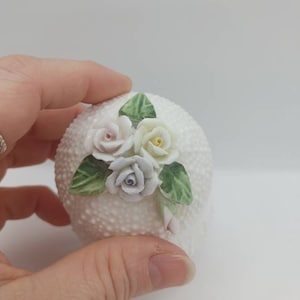 Pretty white vintage trinket box. Porcelain flowers on the top of the lid. The body of the trinket box has a bumpy texture. Lidded + White.