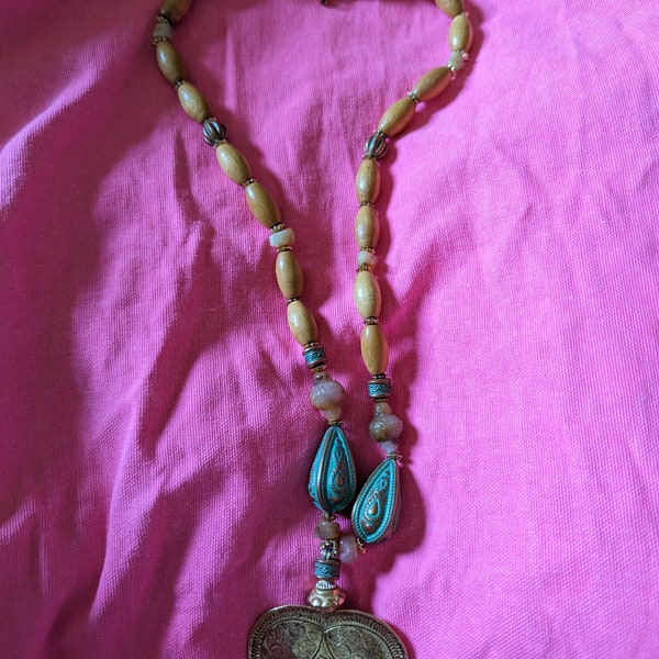 This is necklace with a golden colored heart pendant. It is signed LR on the back. It is made of wooden beads. It's a nice solid necklace.