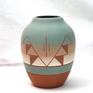 May include: A handcrafted ceramic vase with a rounded shape. The vase features a colour gradient from a terracotta base to a teal upper section. Geometric designs in brown and white adorn the teal section, adding a touch of Southwestern flair.