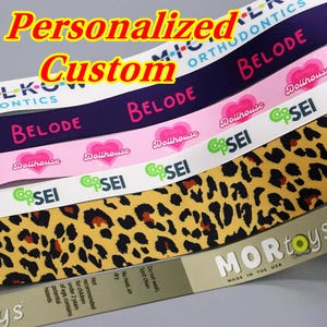 Puede incluir: Una selección de cintas personalizadas con varios diseños y textos. Las cintas muestran textos como "BELODE", "Dollhouse" y "CoopSEI". Una cinta tiene un diseño de estampado de leopardo. Las palabras "Personalized" y "Custom" también son visibles.