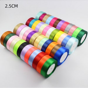 Peut inclure: Un assortiment de rouleaux de ruban de satin de 2,5 cm de large dans différentes couleurs, notamment rouge, bleu, vert, jaune et violet. Les rouleaux sont empilés en forme de pyramide.