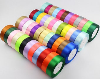 May include: A collection of 2.5 cm wide satin ribbon rolls in various colors, including red, blue, green, yellow, and purple. The rolls are stacked in a pyramid shape.