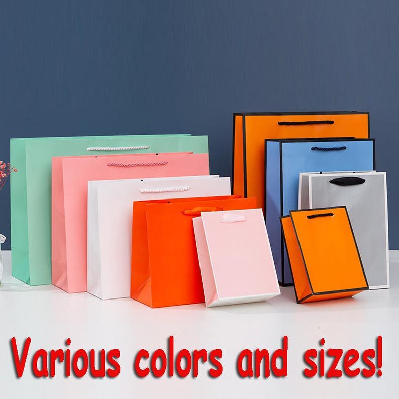 May include: A variety of paper gift bags in different colors and sizes. The bags are arranged in a row from largest to smallest. The colors include green, pink, white, orange, and gray.