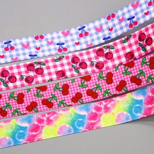 Könnte beinhalten: Vier verschiedene Bandborten mit einem Kirschendruck. Die Bänder sind rosa und blau mit weißen Karomustern. Ein Band hat ein Regenbogenwirbelmuster.