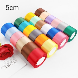 Peut inclure: Un ensemble de 14 rouleaux de ruban de satin de 5 cm de large dans différentes couleurs, notamment rouge, orange, jaune, vert, bleu, violet, rose et marron. Le ruban est disposé en cercle, les extrémités de chaque rouleau se chevauchant.