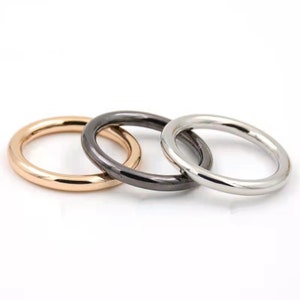 May include: Three metal rings in different finishes: gold, black, and silver. The rings are stacked on top of each other.