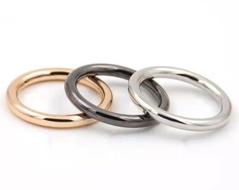 May include: Three metal rings in different finishes: gold, black, and silver. The rings are stacked on top of each other.