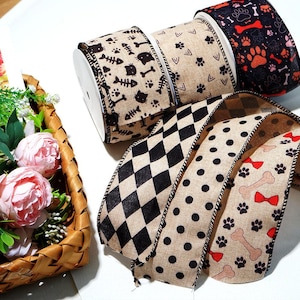 May include: Several decorative ribbons with diverse patterns. Designs include black cat silhouettes with fish bones, paw prints, and dog bones with red bows. The ribbons are on white spools and have a natural, textured appearance.