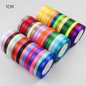 Peut inclure: Assortiment de 25 bobines de ruban de satin de 1 cm de large dans différentes couleurs, notamment rouge, bleu, vert, jaune et violet. Le ruban est enroulé autour de bobines avec des centres blancs.