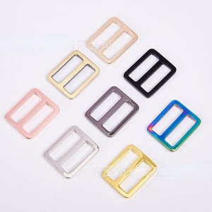 May include: Assortment of eight metal slider buckles in various colors, including gold, silver, black, rose gold, and rainbow.