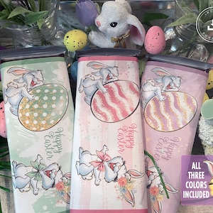 Puede incluir: Tres envoltorios de barra de chocolate de Pascua imprimibles con un conejito sosteniendo un huevo. Los envoltorios son de color verde, rosa y morado con el texto "Feliz Pascua" en cada uno.