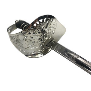May include: A silver sword with a decorative hilt and a black grip. The blade is engraved with a floral design.