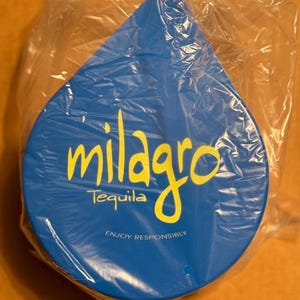 May include: A blue, teardrop-shaped container with the words "Milagro Tequila" and "Enjoy Responsibly" printed on it.