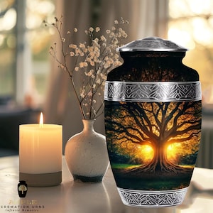 May include: A black cremation urn featuring a tree of life design, with a silver lid and decorative bands. A lit candle and a small vase with flowers are in the background. The urn has the text "APPLE CREMATION URNS Infinite Memories".