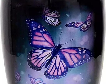 Puede incluir: Una urna negra con acabado brillante, adornada con un diseño de mariposas en tonos rosa, morado y azul. Las mariposas parecen flotar sobre un fondo degradado.