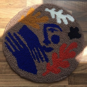 May include: A round rug with a brown background and colorful abstract shapes in blue, red, yellow, and white.