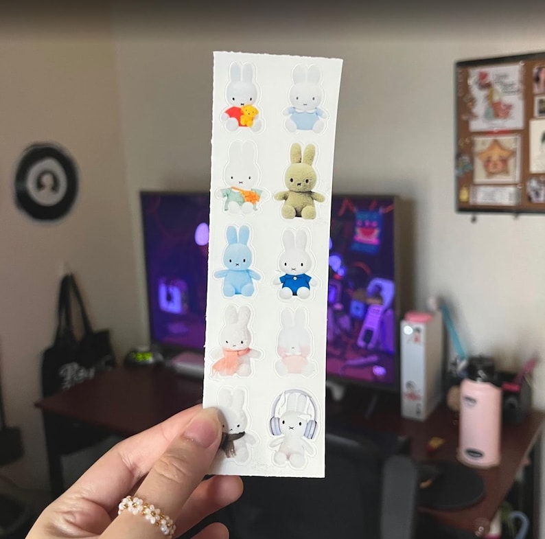 May include: A vertical sticker sheet featuring ten individual illustrations of white rabbits in various outfits and poses, including one wearing headphones, one with a scarf, and others in colorful shirts, arranged in two columns on a white background.