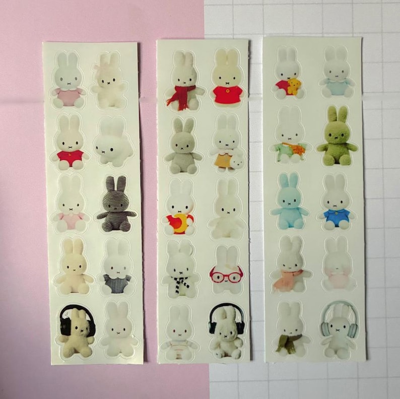 May include: Three vertical sticker sheets featuring a collection of small white rabbit figures in various outfits and poses. The rabbits are depicted wearing accessories like scarves, glasses, and headphones, or holding items, presented on a white background.