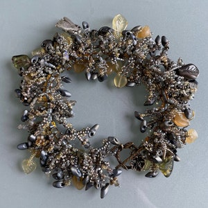 May include: A silver and gold beaded bracelet with a variety of charms, including leaves, flowers, and a bird. The bracelet is made with a variety of different beads, including glass, metal, and plastic.