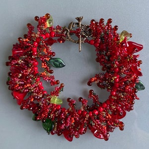 May include: A red, green, and gold beaded bracelet with a floral design. The bracelet is made of small beads and has a clasp closure.