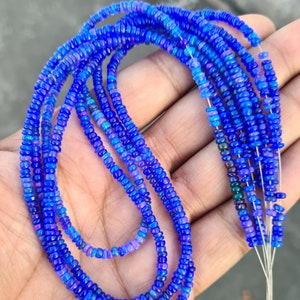 May include: Strands of vibrant blue opal beads. The beads are small, round, and strung together, creating a flowing, layered effect. The opals have a mix of blue and purple hues, with a subtle shimmer. The beads are held in a hand.