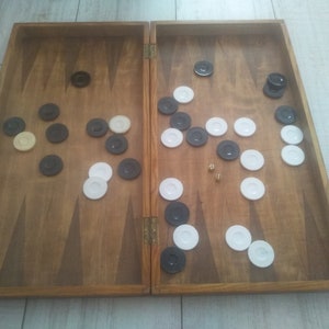 May include: A wooden backgammon board with black and white counters. The board is open and the counters are arranged in a playing pattern.