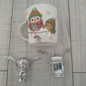 Könnte beinhalten: Zwei silberne Tee-Infuser, einer in Form eines Affen und der andere in Form eines Roboters, auf einer Holzoberfläche.