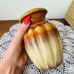 May include: A vintage ceramic vase with a ribbed design. The vase features a gradient of colors, transitioning from a light beige at the base to shades of brown and yellow at the top. The vase has a rounded body and a slightly flared rim.