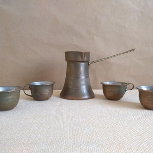 May include: A set of four copper mugs and a copper coffee pot with a long handle. The mugs and pot have a hammered finish and are a traditional style.