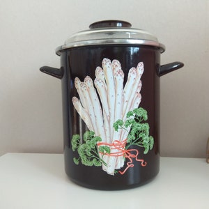 Peut inclure: Une casserole en émail noir avec un couvercle blanc et un motif d'asperges attachées avec un ruban rouge. La casserole a deux poignées sur les côtés.